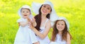 Portrait of happy smiling mother with two daughters children wearing summer straw hats on the grass in park Royalty Free Stock Photo