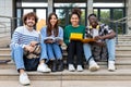 Portrait of happy and smiling multiracial group of college student friends looking at camera sitting on stairs. Royalty Free Stock Photo