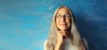 Portrait of happy smiling pensive middle-aged woman in eyeglasses looking away. Gray-haired female thinking on blue background Royalty Free Stock Photo