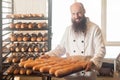 Portrait of happy smiling proud young adult baker with long beard in white uniform standing in his workplace and holding full tray