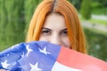 Portrait of happy smiling red haired girl hiding her face behind USA national flag. International day of democracy concept Royalty Free Stock Photo