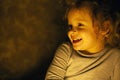 Portrait of a happy and smiling red-haired little girl in the warm rays yellow of a lamp in dark room