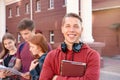 Portrait of happy smiling teenage boy with books and headphones against a group of students near university Royalty Free Stock Photo