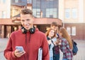 Portrait of happy smiling teenage boy checking his phone against a group of students near university Royalty Free Stock Photo