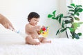 Portrait of happy smiling toddle baby girl sit on fluffy white rug with mother hand hold dusting powder bottle, mom apply talcum Royalty Free Stock Photo