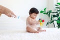 Portrait of happy smiling toddle baby girl sit on fluffy white rug with mother hand hold dusting powder bottle, mom apply talcum Royalty Free Stock Photo