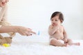 Portrait of happy smiling toddle baby girl sit on fluffy white rug with mother hand hold dusting powder bottle, mom apply talcum Royalty Free Stock Photo