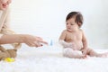 Portrait of happy smiling toddle baby girl sit on fluffy white rug with mother hand hold dusting powder bottle, mom apply talcum Royalty Free Stock Photo