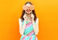 Portrait happy smiling woman hiding her eyes with two lollipop in colorful striped dress on orange wall Royalty Free Stock Photo