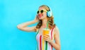 Portrait happy smiling woman holding cup of juice listening to music in wireless headphones on colorful blue Royalty Free Stock Photo