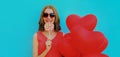 happy smiling woman holding lollipop and bunch of red heart shaped balloons wearing a sunglasses on a blue background Royalty Free Stock Photo