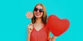 Happy smiling woman holding lollipop and bunch of red heart shaped balloons wearing a sunglasses on a blue background Royalty Free Stock Photo