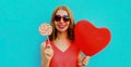 Happy smiling woman holding lollipop and bunch of red heart shaped balloons wearing a sunglasses on a blue background Royalty Free Stock Photo