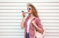 Portrait happy smiling woman holding phone using voice command recorder or calling, wearing summer round straw hat with bag