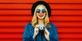 Portrait of happy smiling woman with retro camera wearing blue faux fur coat, round hat over red