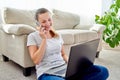 Portrait of happy smiling woman sitting on floor, using laptop and talking on phone at home, copy space Royalty Free Stock Photo
