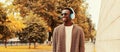 Portrait of happy smiling young african man in headphones listening to music wearing brown knitted cardigan in the city park Royalty Free Stock Photo