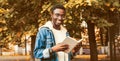 Portrait of happy smiling young african man student reading a book wearing eyeglasses in autumn city park Royalty Free Stock Photo