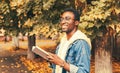 Portrait of happy smiling young african man student reading a book wearing eyeglasses in autumn city park Royalty Free Stock Photo