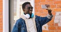 Portrait happy smiling young african man taking selfie by smartphone listening to music in headphones on a city street Royalty Free Stock Photo