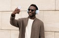 Portrait happy smiling young african man taking a selfie by smartphone while listening to music in headphones on a city street Royalty Free Stock Photo