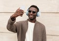 Portrait happy smiling young african man taking a selfie by smartphone while listening to music in headphones on a city street Royalty Free Stock Photo