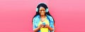 Portrait of happy smiling young african woman in headphones listening to music with smartphone on pink background Royalty Free Stock Photo