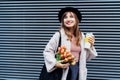 Portrait of happy, smiling young fashion woman in hat holding reusable coffee cup and bouquet of tulip flowers on the