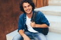 Portrait of happy smiling young man student ith backpack sitting at concrete stairs on the city street. Businessman freelancer Royalty Free Stock Photo