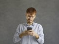 Portrait of smiling young man using mobile phone standing over grey studio wall Royalty Free Stock Photo