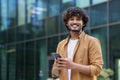 Portrait of a happy and smiling young Muslim man standing on a city street using a mobile phone and looking confidently Royalty Free Stock Photo