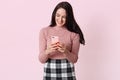 Portrait of happy smiling young woman in casual shirt and checkered skirt, using mobile phone, typing messages or checking social Royalty Free Stock Photo