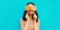 Portrait happy smiling young woman covering her eyes with lollipop on blue background Royalty Free Stock Photo