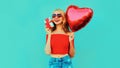 portrait happy smiling young woman holding gift box, red heart shaped air balloon on colorful blue Royalty Free Stock Photo