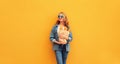 Portrait of happy smiling young woman holding grocery shopping paper bag with long white bread baguette on orange background Royalty Free Stock Photo