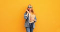 Portrait of happy smiling young woman holding grocery shopping paper bag with long white bread baguette on orange background Royalty Free Stock Photo