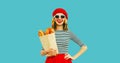Portrait of happy smiling young woman holding grocery shopping paper bag with long white loaf bread baguette wearing french red