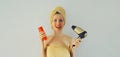 Portrait of happy smiling young woman holding hair dryer and bottle of shampoo while drying wet hair in wrapped bath towel and Royalty Free Stock Photo