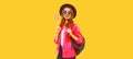 Portrait of happy smiling young woman holding lollipop wearing pink jacket, black round hat on yellow background Royalty Free Stock Photo