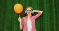 Portrait happy smiling young woman listening to music in headphones with orange balloon lying on the grass background in summer Royalty Free Stock Photo