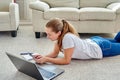 Portrait of happy smiling young woman lying on floor with laptop and using smartphone at home, copy space Royalty Free Stock Photo