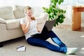 Portrait of happy smiling young woman lying on floor, using laptop and talking on phone at home, copy space. Royalty Free Stock Photo