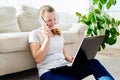 Portrait of happy smiling young woman lying on floor, using laptop and talking on phone at home, copy space. Royalty Free Stock Photo