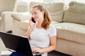 Portrait of happy smiling young woman lying on floor, using laptop and talking on phone at home, copy space. Royalty Free Stock Photo