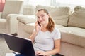 Portrait of happy smiling young woman lying on floor, using laptop and talking on phone at home, copy space. Royalty Free Stock Photo