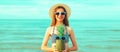 Portrait of happy smiling young woman with pineapple wearing straw hat on the beach on sea background at summer day Royalty Free Stock Photo