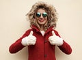 Portrait happy smiling young woman showing thumbs up wearing red jacket with fur hood and white mittens Royalty Free Stock Photo