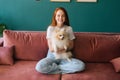 Portrait of happy smiling young woman sitting on comfortable sofa cuddling pretty small white spitz pet dog at apartment Royalty Free Stock Photo