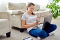 Portrait of happy smiling young woman sitting on floor with laptop and using smartphone at home, copy space