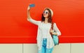 Portrait happy smiling young woman taking a selfie by smartphone wearing summer straw round hat, backpack on blue background Royalty Free Stock Photo